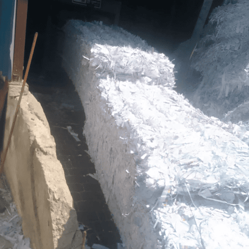 Gestion des déchets 69 Une scène d'intérieur d'entrepôt montrant une importante collection de déchets de papier blanc recyclé préparés pour le transport. Plusieurs grosses balles de papier blanc compactées sont alignées co