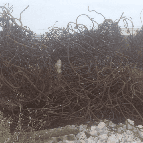 Gestion des déchets 66 Une vue détaillée en gros plan et en plongée de plusieurs vieilles barres omnibus en cuivre ternies et perforées, superposées sur le sol rugueux et poussiéreux d'un atelier. Le métal présente une for