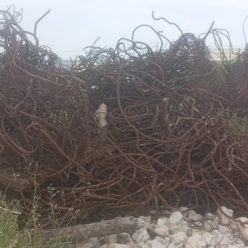 Gestion des déchets 64 Une vue détaillée en gros plan et en plongée de plusieurs vieilles barres omnibus en cuivre ternies et perforées, superposées sur le sol rugueux et poussiéreux d'un atelier. Le métal présente une for